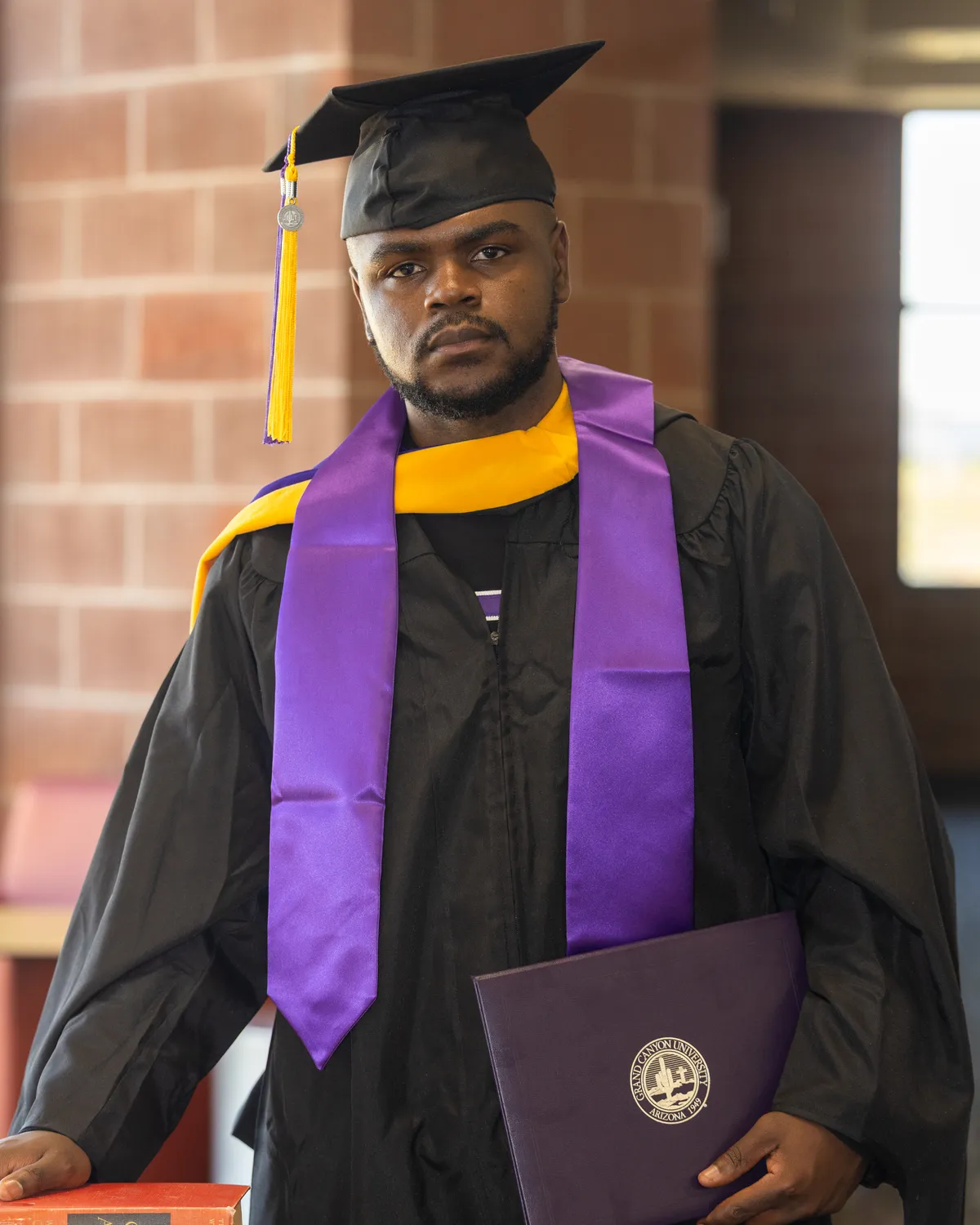 Armand Junior Dongmo Notue in graduation cap and gown, holding his Grand Canyon University diploma